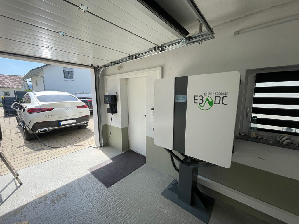 Weißes Elektroauto steht vor der Garage und wird geladen.